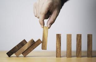 Hand pull out wooden block to prevent and stop falling domino ,It is a symbol of protection against damage or stop loss for crisis management concept. photo