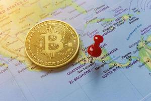 A red pin is pinned on the world map of El Salvador and there is a bitcoin next to it. photo