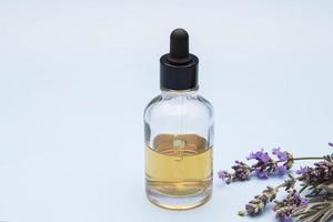 A glass bottle with a dropper filled with liquid on a blue background with lavender flowers photo