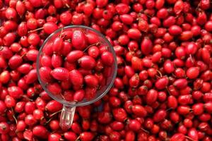 Rose hip or rosehip inside of the glass and over the table. Empty space for copy paste. Backgrounds and textures. Red vibrant colors. Cinematic. Wild fruits and healthy food. photo