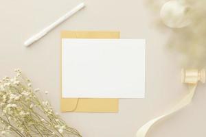 maqueta de invitación de tarjeta de felicitación en blanco 5x7 en sobre con flores secas y cinta sobre fondo de papel, capa plana, maqueta foto