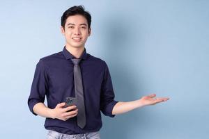 Portrait of young Asian businessman using smartphone on blue background photo