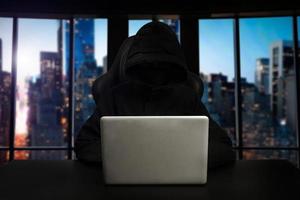 Hacker using computer with digital interface while sitting at desk of blurry interior. Hacking and thief concept. photo