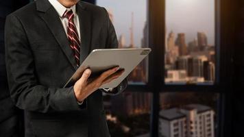 Business man in white shirt using or browsing internet on digital tablet computer with blurred modern office background photo