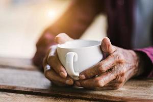 manos de anciano sosteniendo una taza de café en la mesa de madera.