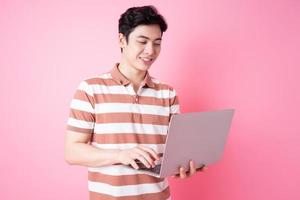 Portrait of young Asian man using laptop on pink background photo