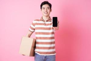 Image of young Asian man holding cardboard on pink background photo