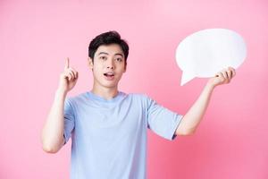 Image of young Asian man holding message bubble on pink background photo