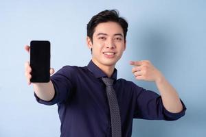retrato de un joven hombre de negocios asiático usando un teléfono inteligente con fondo azul foto