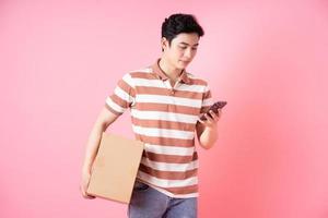 Image of young Asian man holding cardboard on pink background photo