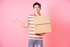 Image of young Asian man holding cardboard on pink background photo