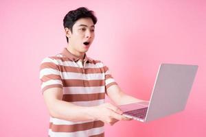 Portrait of young Asian man using laptop on pink background photo