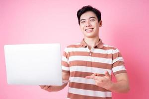 Portrait of young Asian man using laptop on pink background photo