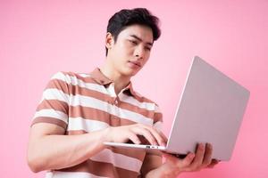 retrato de un joven asiático usando una laptop con fondo rosa foto