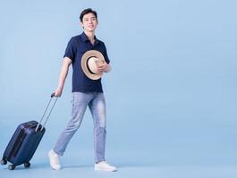Image of young Asian man holding suitcase on blue background, travel concept photo