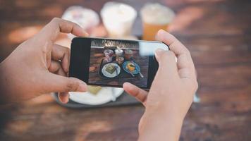 manos de mujer tomando fotografías de alimentos en su teléfono móvil, mujer cliente que usa un teléfono inteligente toma una foto de comida para compartir con sus amigos en la cafetería y en la tienda del restaurante. teléfono inteligente digital de tecnología