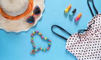 Summer composition. Sunglasses, hat, polka dot swimsuit, nail polish and a heart made of beads on a blue background with copy space. Vacation concept., flat lay. photo