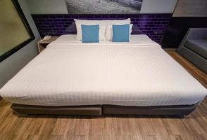 white bed sheet in cozy room. blue pillow . wooden plank floor and beauty decoration for welcome guest in hotel. photo