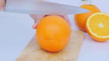 Zoomen Sie heran, um eine reife Orangenfrucht mit goldgelber Schale zu halbieren und in Scheiben zu schneiden. isoliert auf weißem Hintergrund mit Schatten. video
