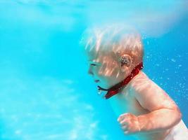 Little boy infant with red butterfly diving underwater in swimming pool, learn to swim. Sport and vacation concept photo