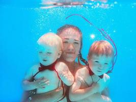 mujer caucásica con niños pequeños en mariposas rojas buceando bajo el agua en la piscina, aprende a nadar. concepto de deporte, familia, amor y vacaciones foto