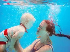 bella joven con un lindo niño en mariposa, su hijo, bajo el agua en la piscina, aprende a nadar. concepto de deporte, familia, amor y vacaciones foto