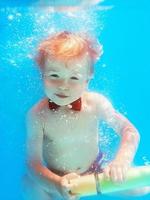 niño pequeño con mariposa roja buceando bajo el agua en la piscina, aprende a nadar. concepto de deporte y vacaciones foto