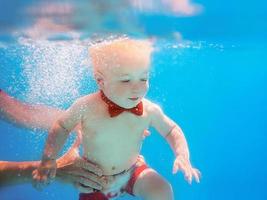 Little boy infant with red butterfly diving underwater in swimming pool, learn to swim. Sport and vacation concept