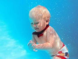 niño pequeño con mariposa roja buceando bajo el agua en la piscina, aprende a nadar. concepto de deporte y vacaciones foto