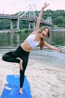 young fit woman in sportswear starting yoga and have troubles with yoga asanas outdoor on the beach by the river. Yoga and sport concept