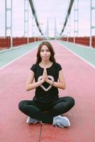 beautiful, sporty, fit, young caucasian woman in sportswear and sneakers sitting in lotus pose on the bridge. Sport, activity, yoga, urban lifestyle concept photo