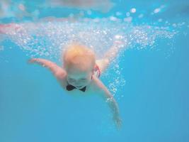 niño pequeño con mariposa roja buceando bajo el agua en la piscina, aprende a nadar. concepto de deporte y vacaciones foto