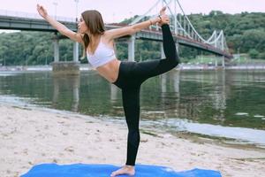 young fit woman in sportswear in different yoga asanas outdoor on the beach by the river. Yoga and sport concept