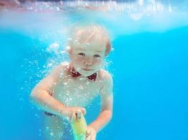 niño pequeño con mariposa roja buceando bajo el agua en la piscina, aprende a nadar. concepto de deporte y vacaciones foto