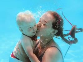 bella joven con un lindo niño en mariposa, su hijo, bajo el agua en la piscina, aprende a nadar. concepto de deporte, familia, amor y vacaciones