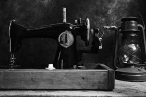 máquina de coser antigua, retro, vintage y una lámpara de queroseno sobre un fondo oscuro de una pared abstracta.
