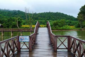 un puente de madera en medio del pantano con un cartel que prohíbe alimentar a los peces y vistas a las montañas y los árboles.