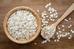 Rolled oats in a wooden cup and spoon on a wooden table, top view. It is a healthy whole grain food. photo