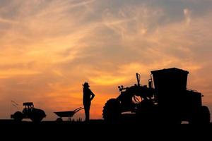 Silhouette of worker and grader at construction site, Road construction worker and compactors with blurred compactors sunset background photo