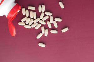 white color medical pills spilling on red background photo