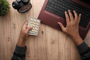 top view of hand holding blister packs and using laptop photo