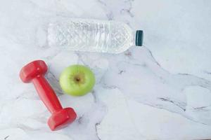 fresh drinking water, apple and a red color dumbbell on table photo