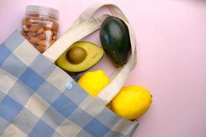 top view of shopping bag, slice of avocado, lemon and almond nut on table photo