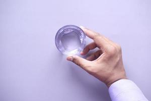 mano sosteniendo un vaso de agua sobre fondo morado foto