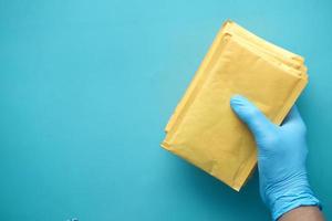 mano en guantes de látex con sobre de burbujas de papel blanco para envío postal. foto