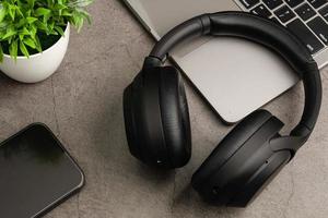 Black headphones on a grey table. Concept of playing music with a smartphone and listening with wireless headphones in the living room and work at home. Close-up, selective focus. Blurred background. photo