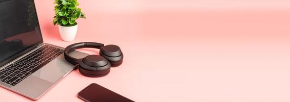 Black headphones on a table. Concept of playing music with a smartphone and listening with wireless headphones in living room and work at home. Copy space for design, selective focus. pink background. photo