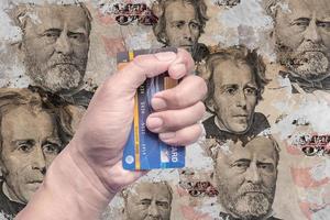 tarjeta de crédito en la mano de un hombre con una foto del dinero en dólares en una pared vieja.