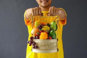 primer plano de una variedad de frutas en la cesta sosteniendo por un hombre sonriente foto