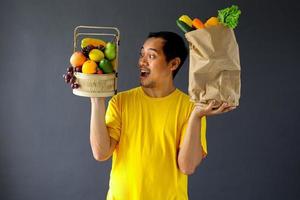 hombre asiático asombrado sosteniendo una cesta de frutas y verduras en una bolsa de compras para el concepto de campaña de estilo de vida saludable